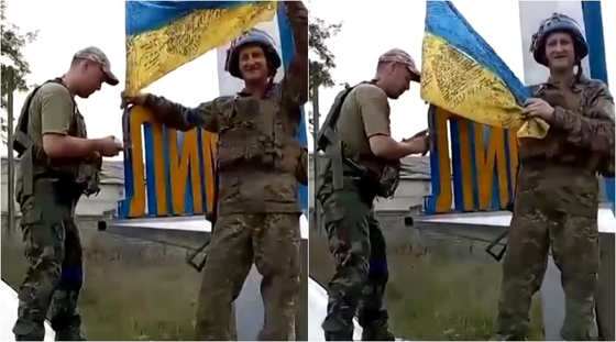우크라이나 군인 2명이 리만 도시 표지판에 국기를 붙이는 모습. 〈사진=로이터통신 홈페이지 캡처/우크라이나 대통령 비서실〉