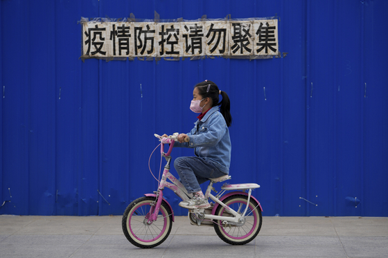 베이징의 한 거주 지역에서 &#34;방역을 위해 모이지 마시오&#34; 라고 쓰인 통보문 아래로 마스크를 한 아이가 자전거를 타고 지나가고 있다. 〈사진=AP, 연합뉴스〉