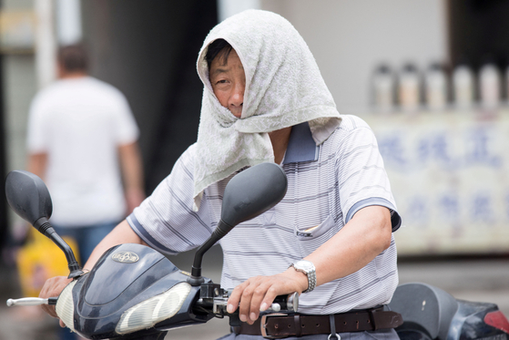 중국에서 한 남성이 뜨거운 햇볕을 피하기 위해 수건을 입에 물고 있다 〈사진=로이터 연합〉