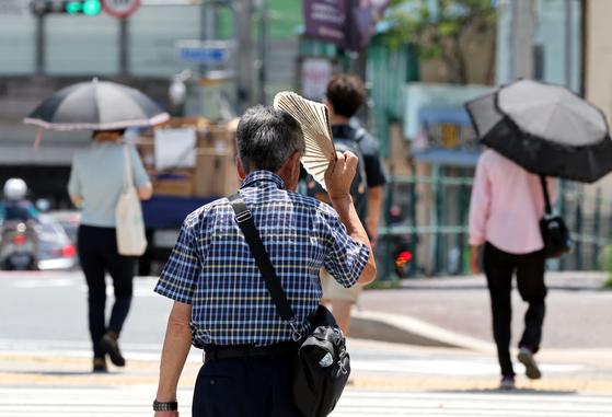 지난달 31일 부산진구 부산시민공원 앞 횡단보도를 시민이 부채를 들고 햇볕을 가리고 있다. 〈사진=연합뉴스〉